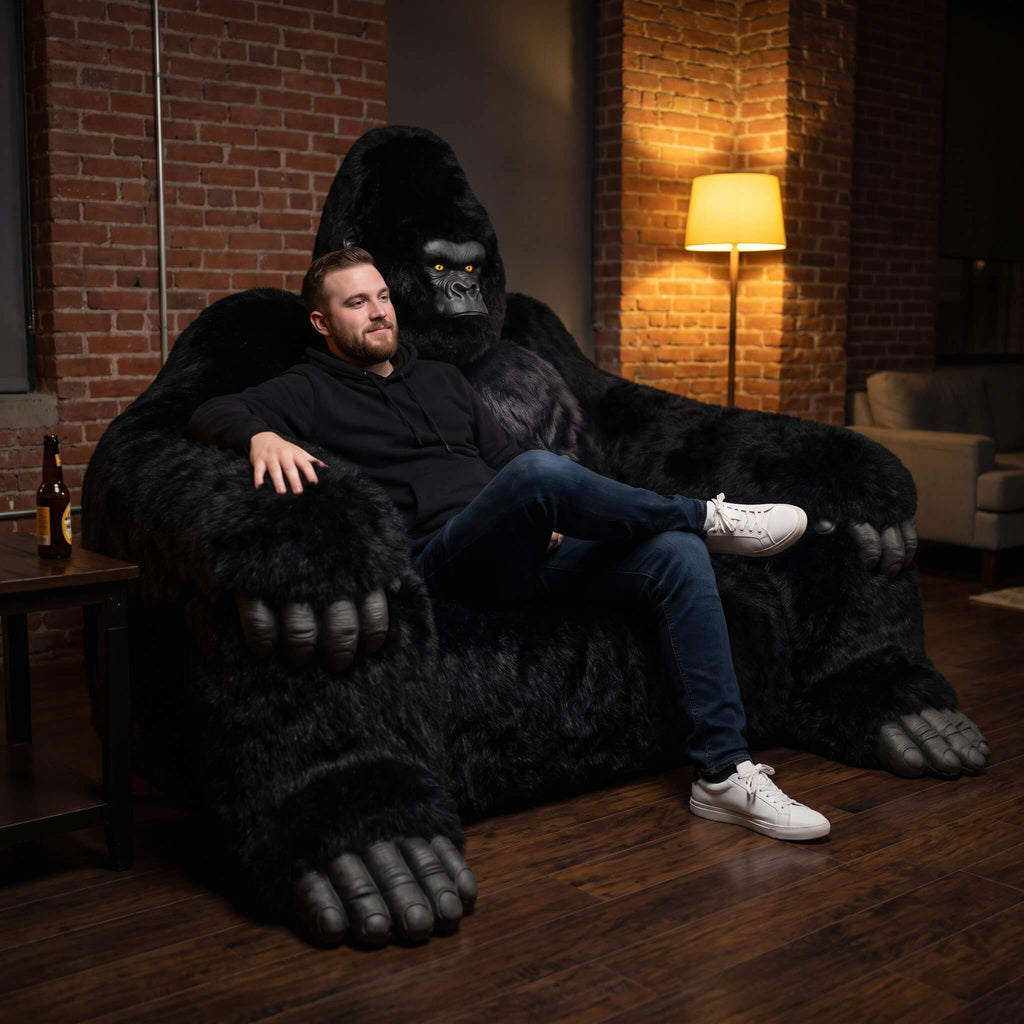 Man sitting on a large black gorilla-shaped chair in a dimly lit room with brick walls.