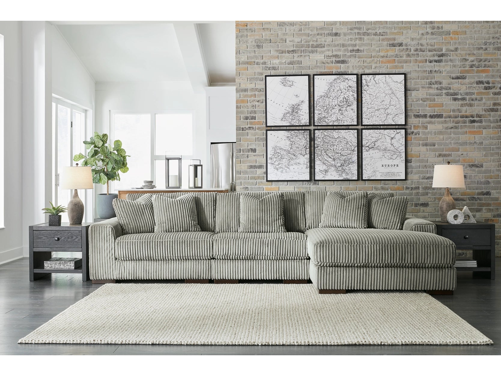 Gray sectional sofa in a living room with a brick wall and framed pictures.