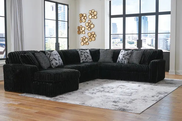 Black sectional sofa in a room with large windows and decorative wall art.