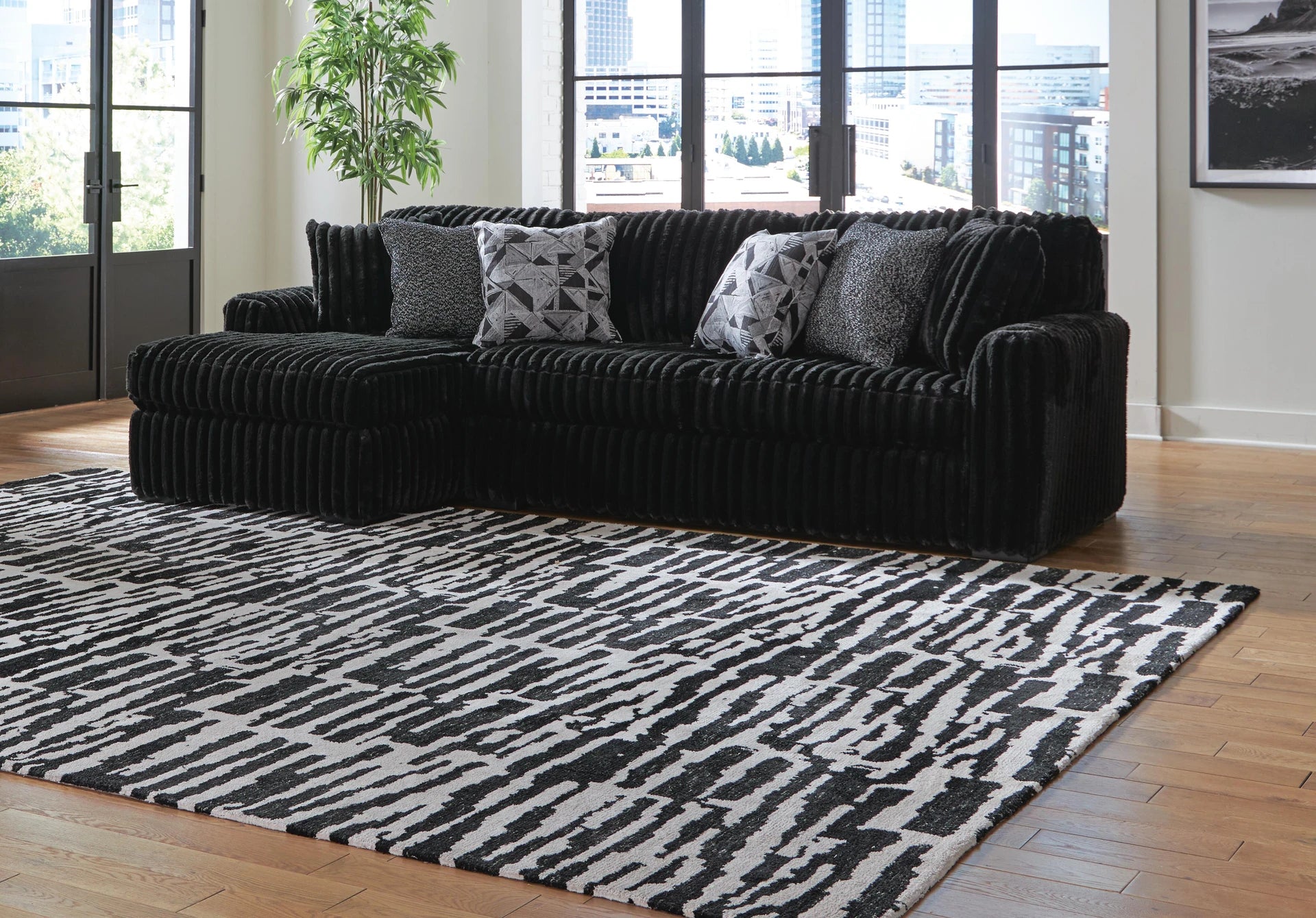 Black sectional sofa with patterned cushions on a black and white rug in a living room.
