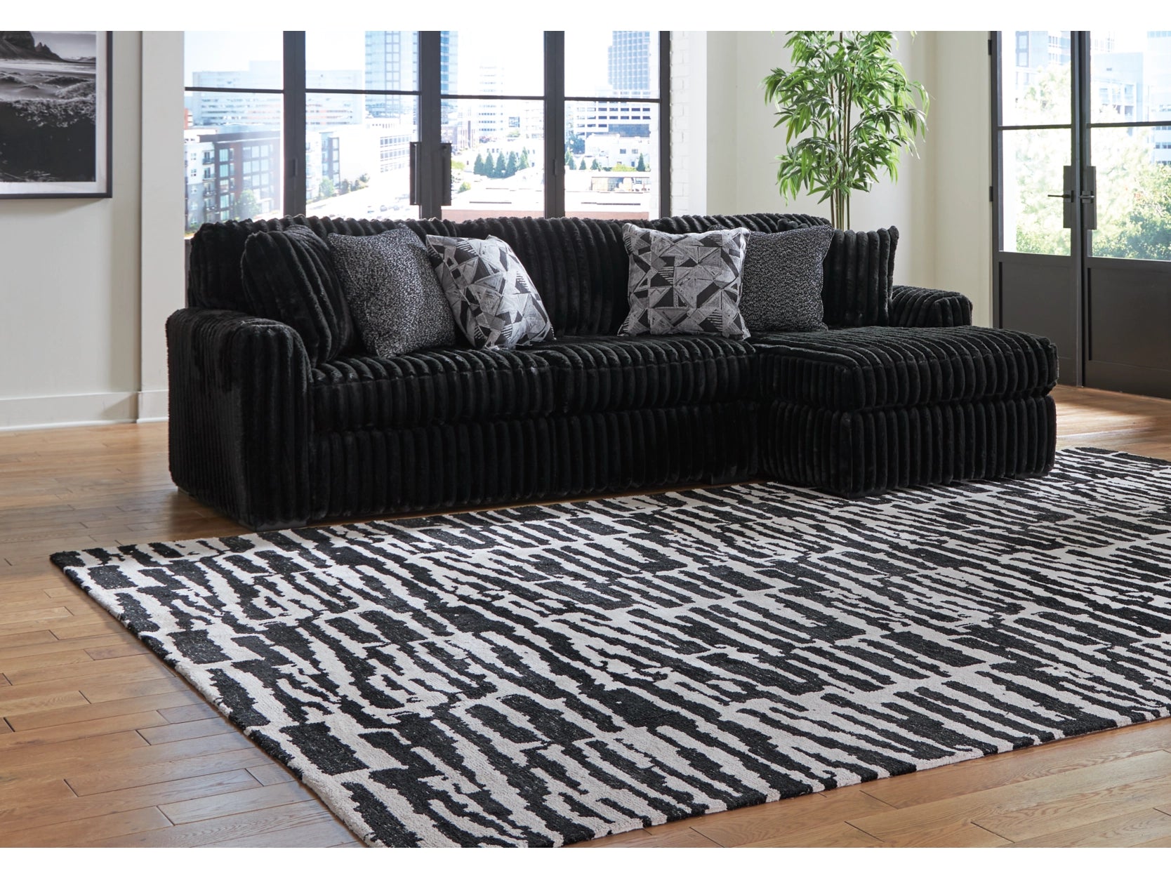 Black sectional sofa with patterned cushions on a black and white rug in a living room.