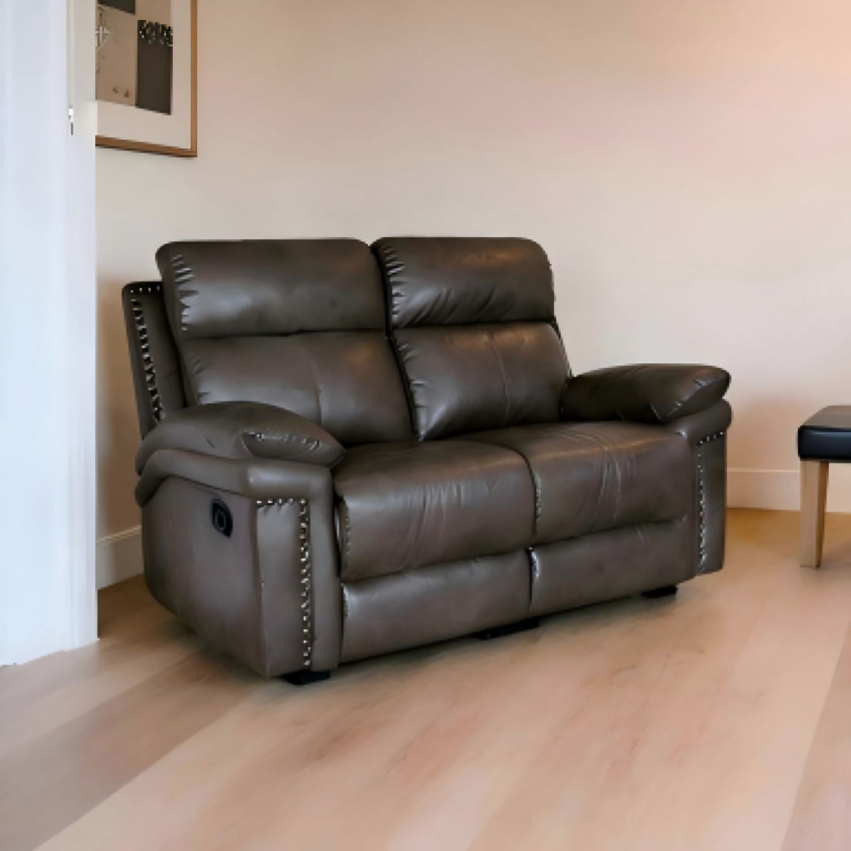 Brown leather recliner sofa in a room with light wood flooring and a white wall.