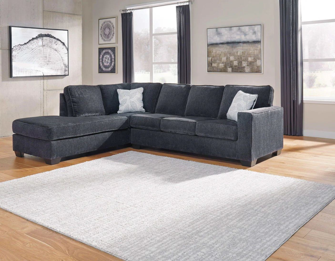 Gray sectional sofa in a living room with large windows and framed artwork on the walls.