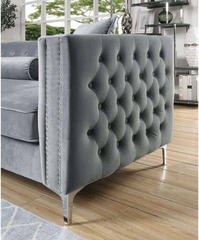 Gray tufted sofa with nailhead trim in a room with wooden flooring and a rug.