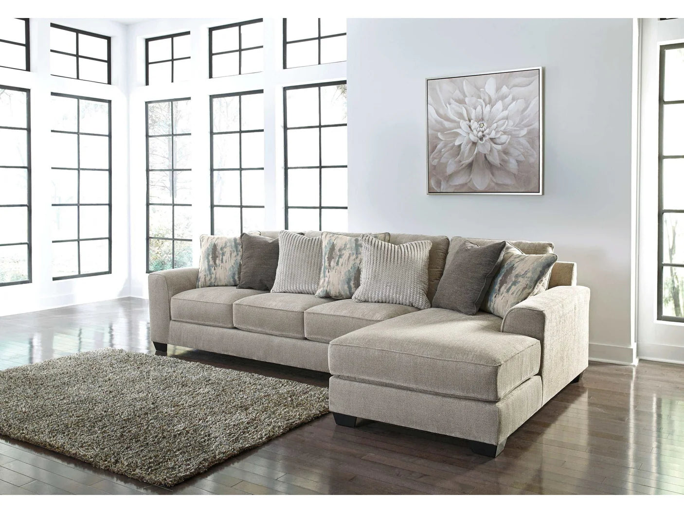 Gray sectional sofa in a room with large windows and a floral painting on the wall.