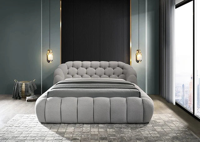 Gray upholstered bed in a modern bedroom with large windows and decorative lighting.