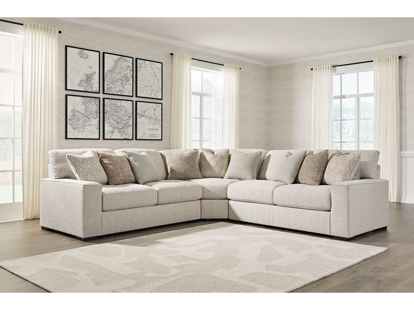 Beige sectional sofa in a living room with large windows and framed maps on the wall.