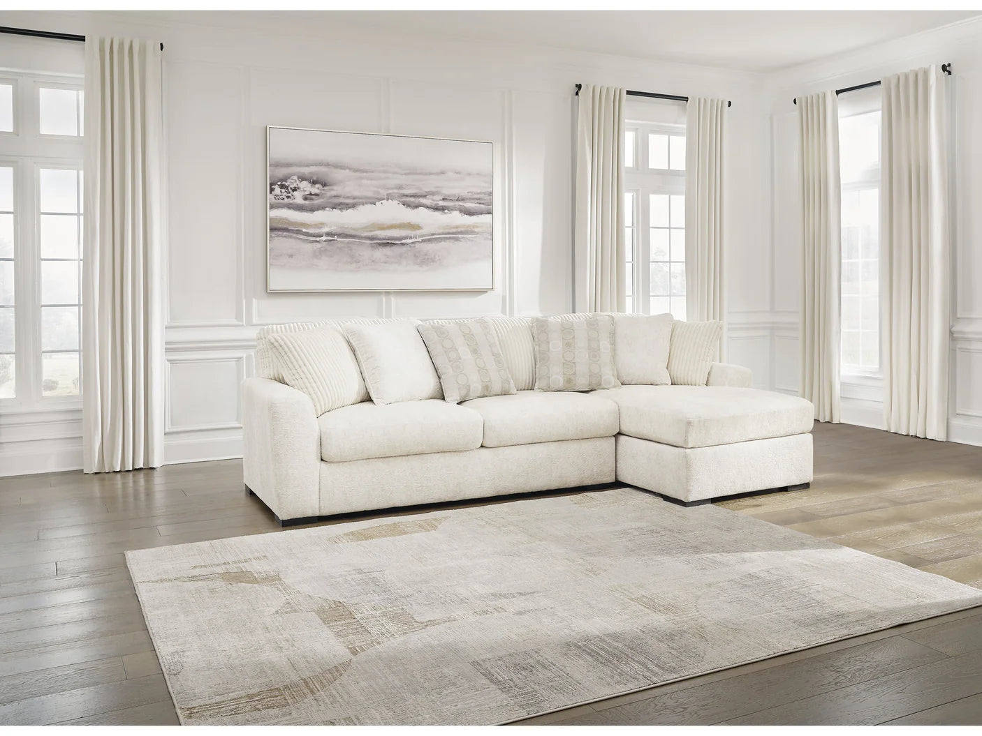 White sectional sofa in a living room with large windows and a painting on the wall.