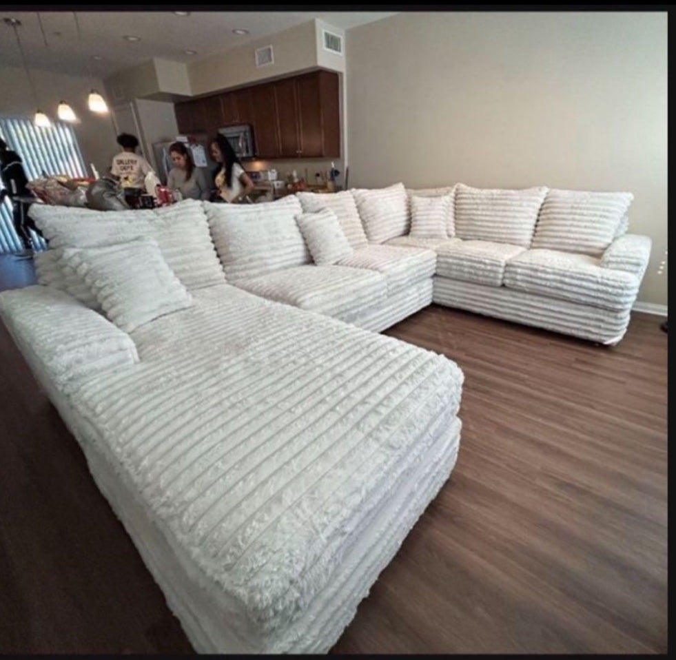 Cream-colored corduroy sectional couch with deep plush cushions and an oversized u-shaped design in a modern living room with wood floors and an open kitchen in the background.