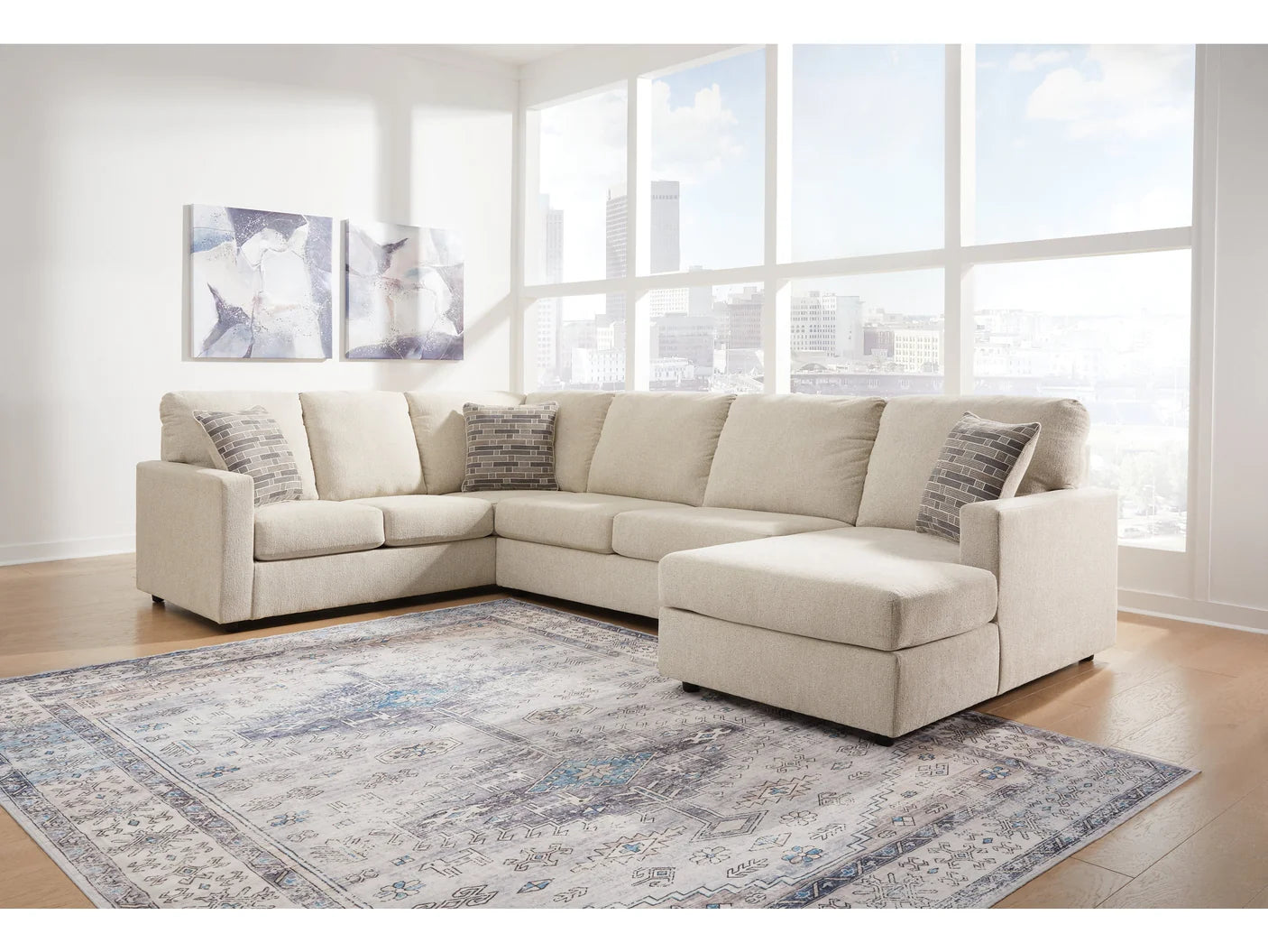 Beige sectional sofa in a living room with large windows and a patterned rug.