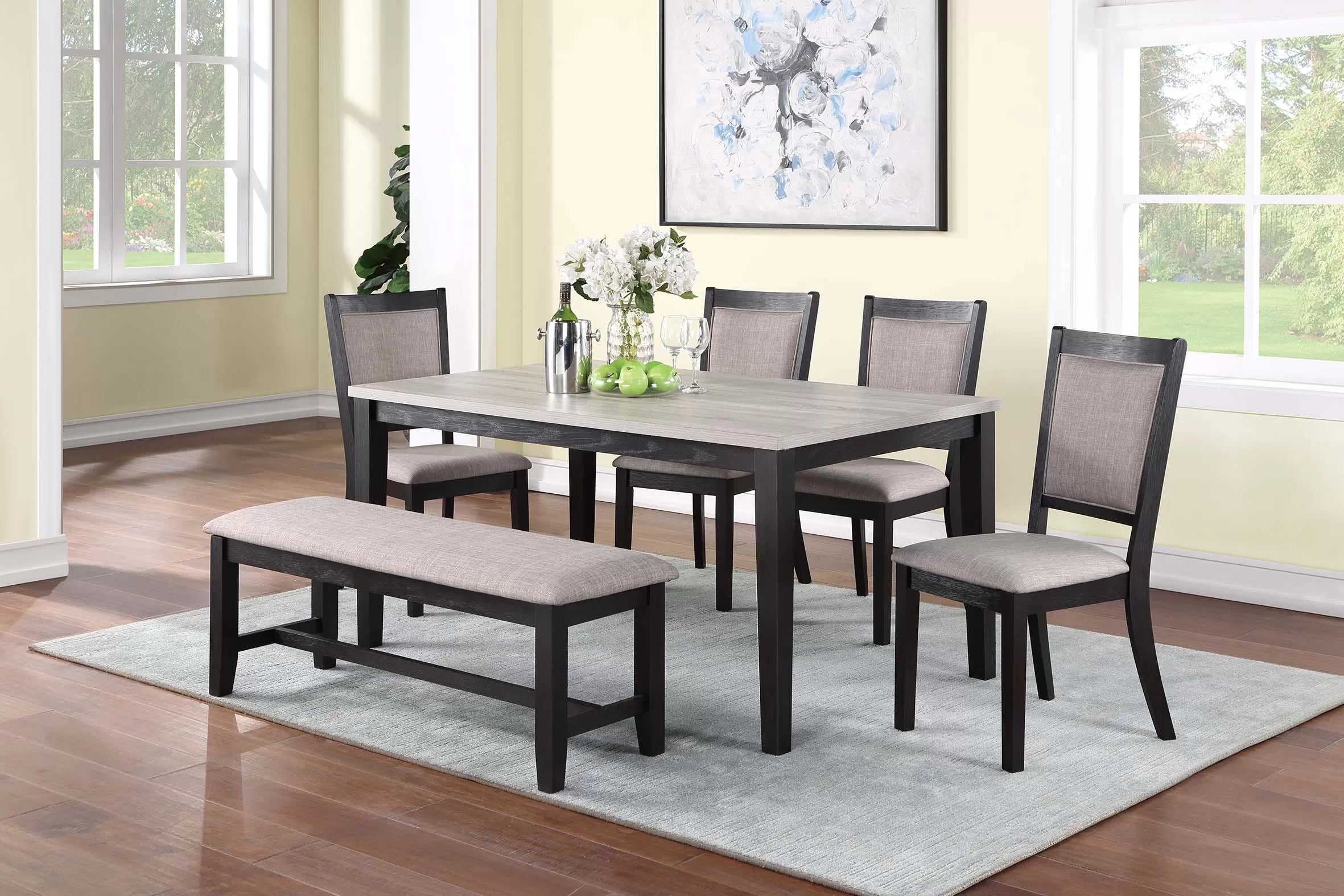 Dining room set with table, chairs, and bench on a rug in a well-lit room.
