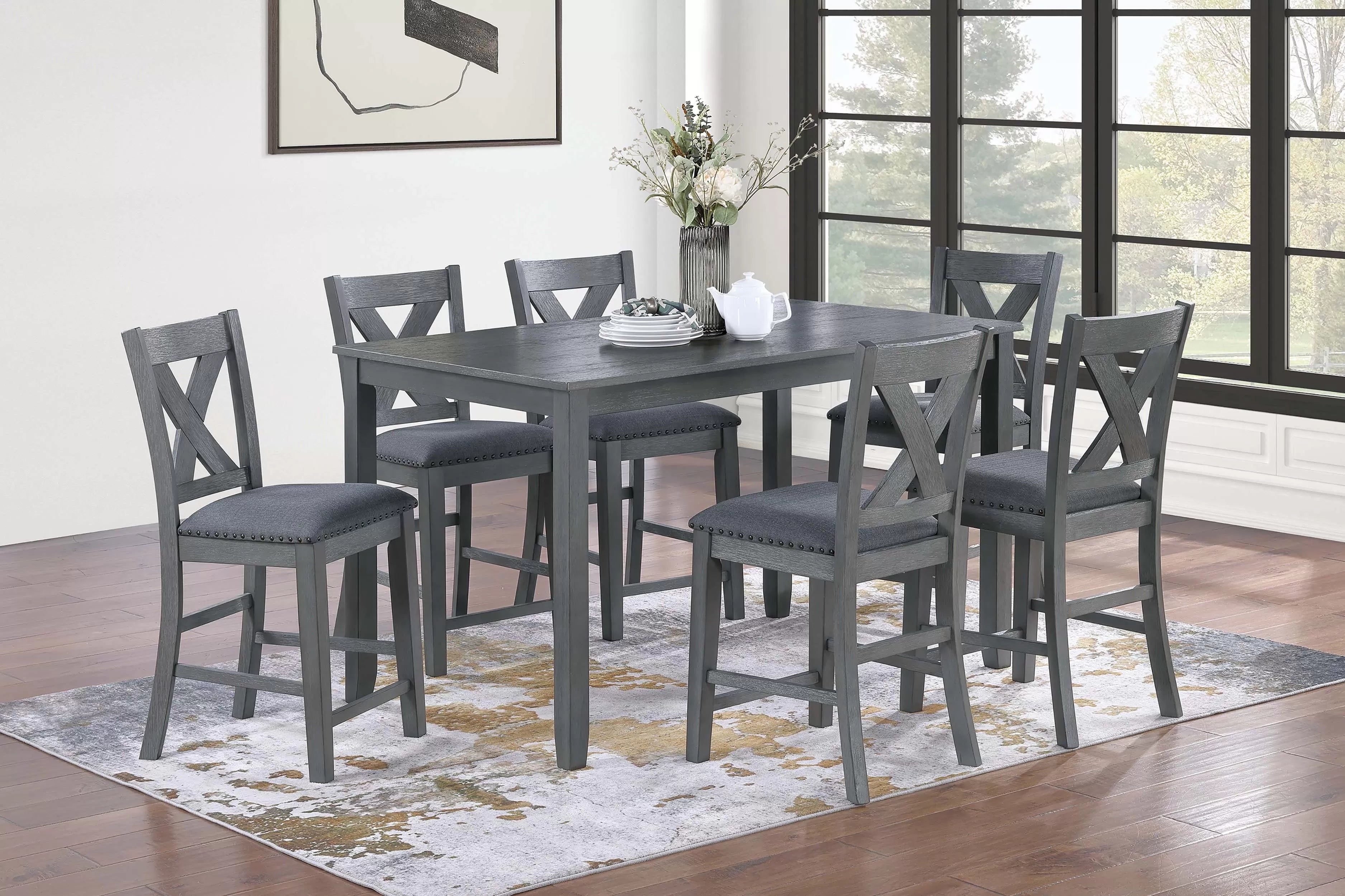 Gray dining table set with six chairs in a room with large windows.