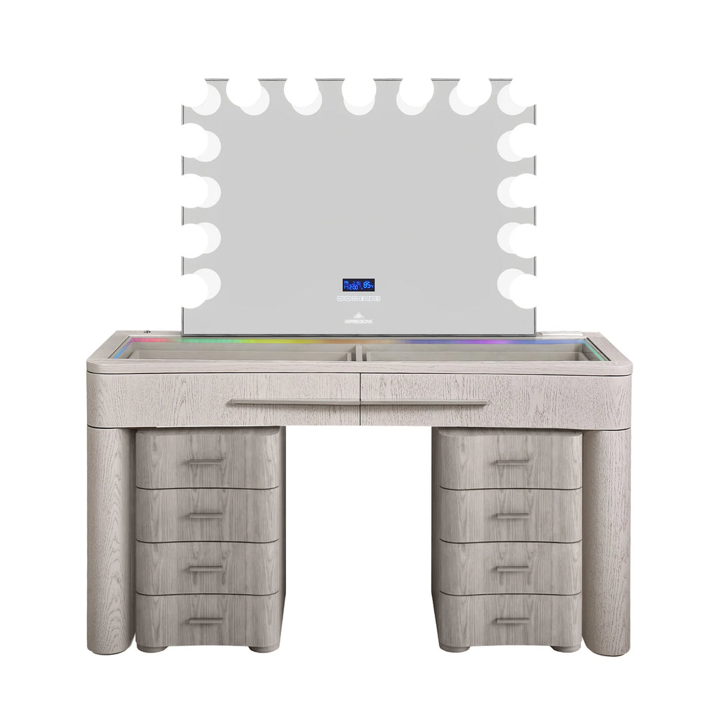 Modern white wood makeup vanity with RGB LED lighting, large Hollywood-style mirror with globe bulbs, glass top surface, and matching drawer storage stools in a white back setting.