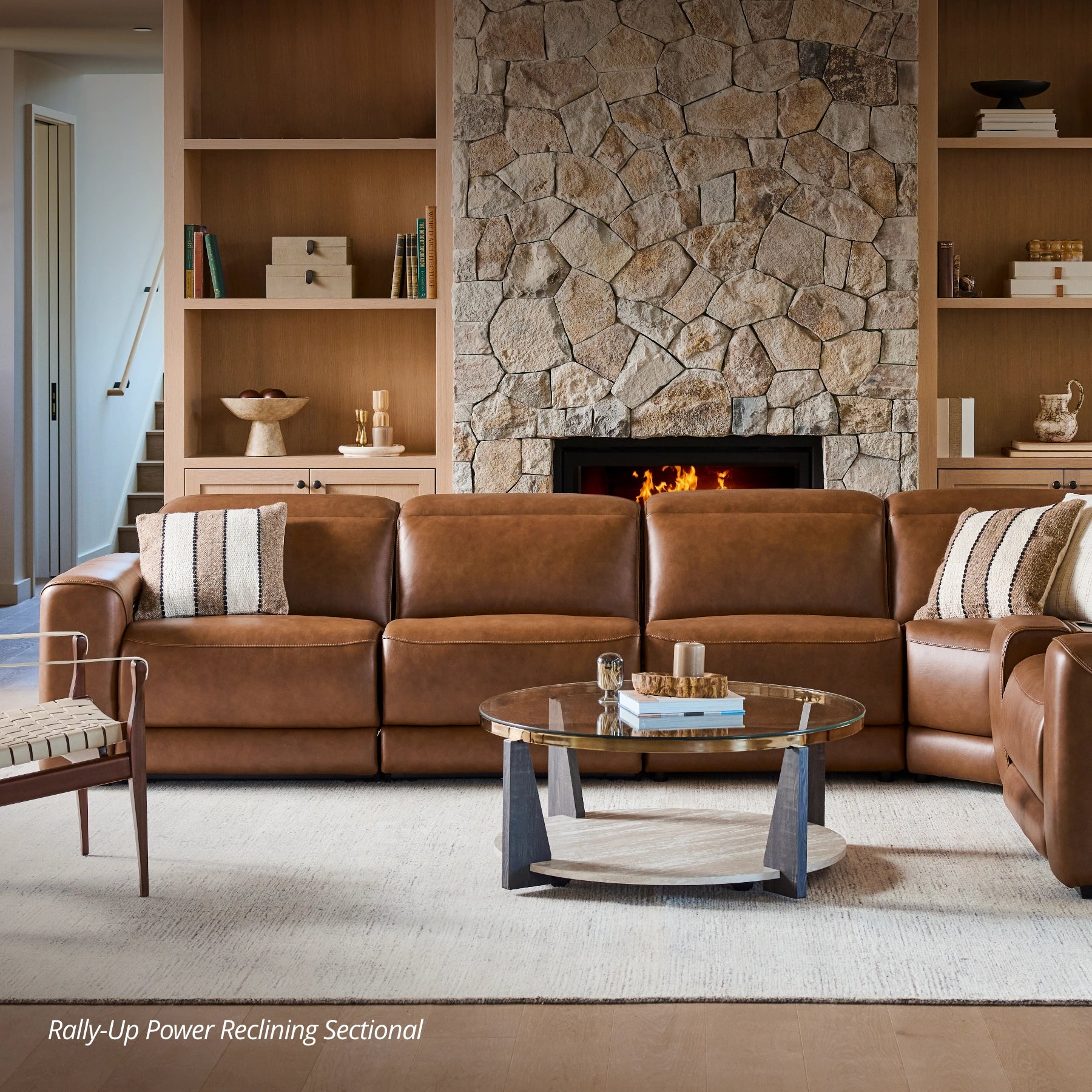 Living room with brown leather sectional sofa, stone fireplace, and bookshelves.