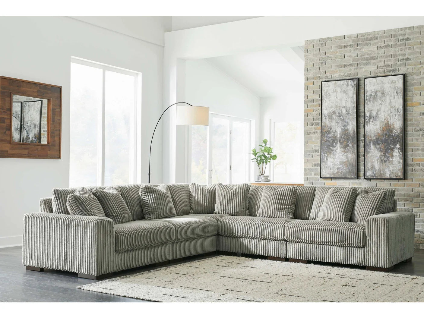 Gray sectional sofa in a living room with a brick wall and large windows.