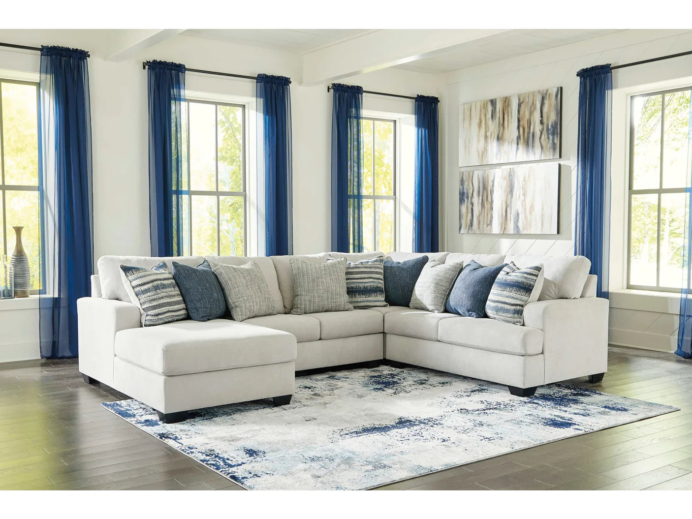 Living room with a white sectional sofa, blue curtains, and a floral rug.