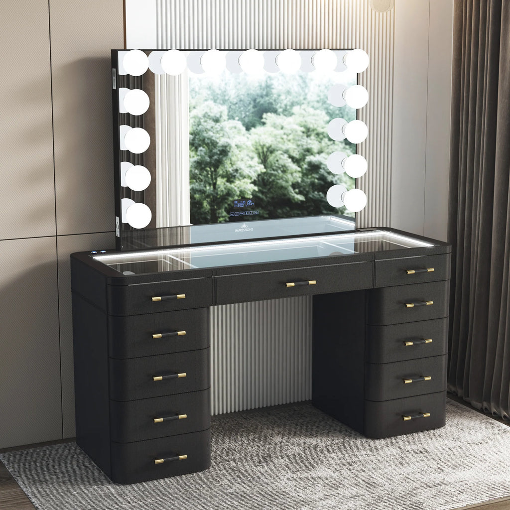 Luxury black makeup vanity set with illuminated Hollywood mirror, glass top storage compartments, LED lighting, and gold drawer handles in a modern bedroom.