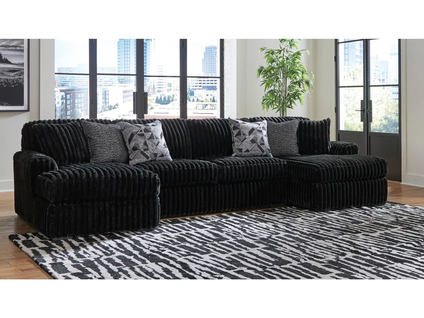 Black sectional sofa with patterned cushions in a room with large windows.