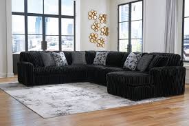 Black sectional sofa in a living room with large windows and decorative elements.