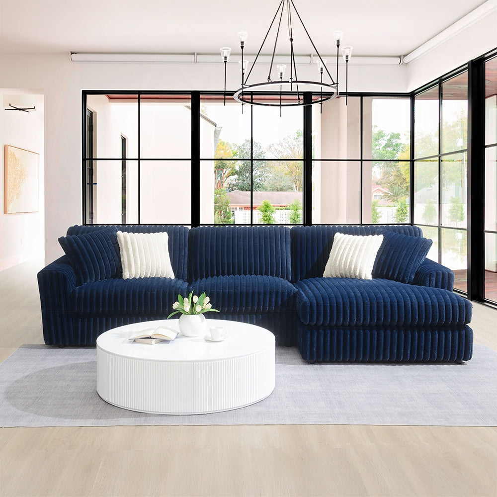 Modern living room with a blue sectional sofa, white coffee table, and large windows.